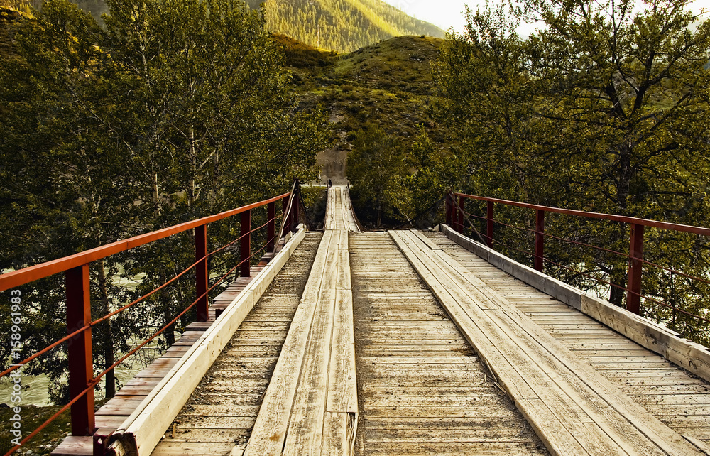 Trekking in the Altai region in the vicinity of the Katun River. Summer. Bridge over Katun river, wood log bridge, mounted with metal cables. Trekking in the Altai region in the vicinity of the Katun River. Summer. Bridge over Katun river, wood log bridge, mounted with metal cables.