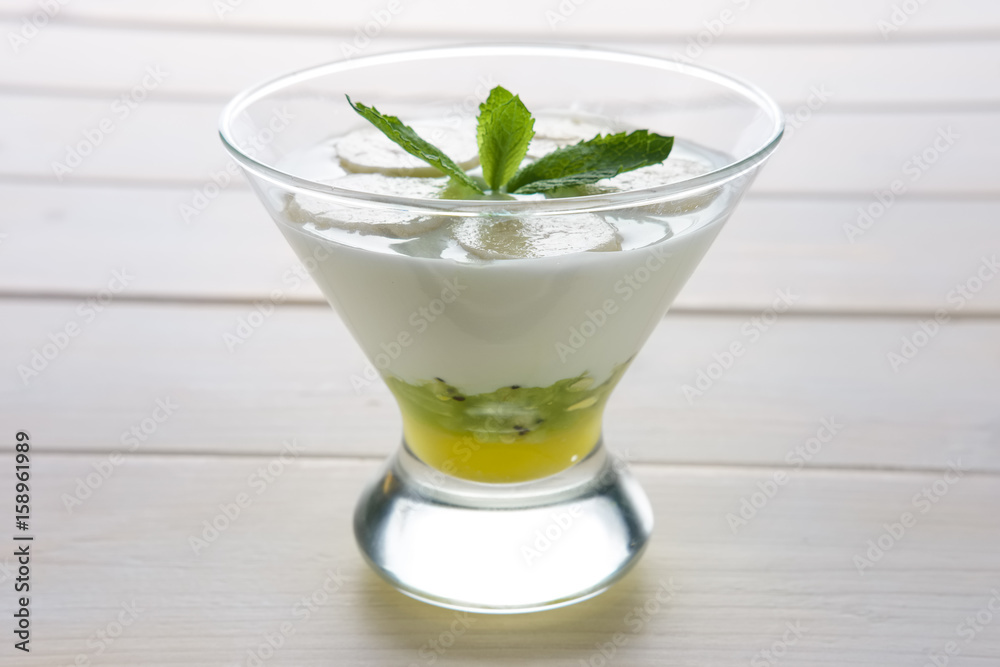 Glass with yogurt with banana and kiwi with honey decorated with mint leaf on top Glass with yogurt with banana and kiwi with honey decorated with mint leaf on top