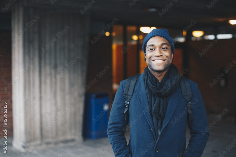Portrait of happy man wearing blue warm clothing and knit hat standing in campus Portrait of happy man wearing blue warm clothing and knit hat standing in campus