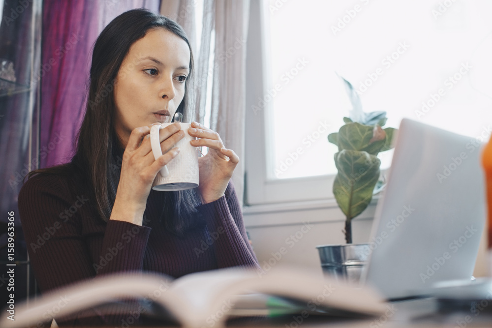 © Maskot - Young woman during coffee break against window in college dorm