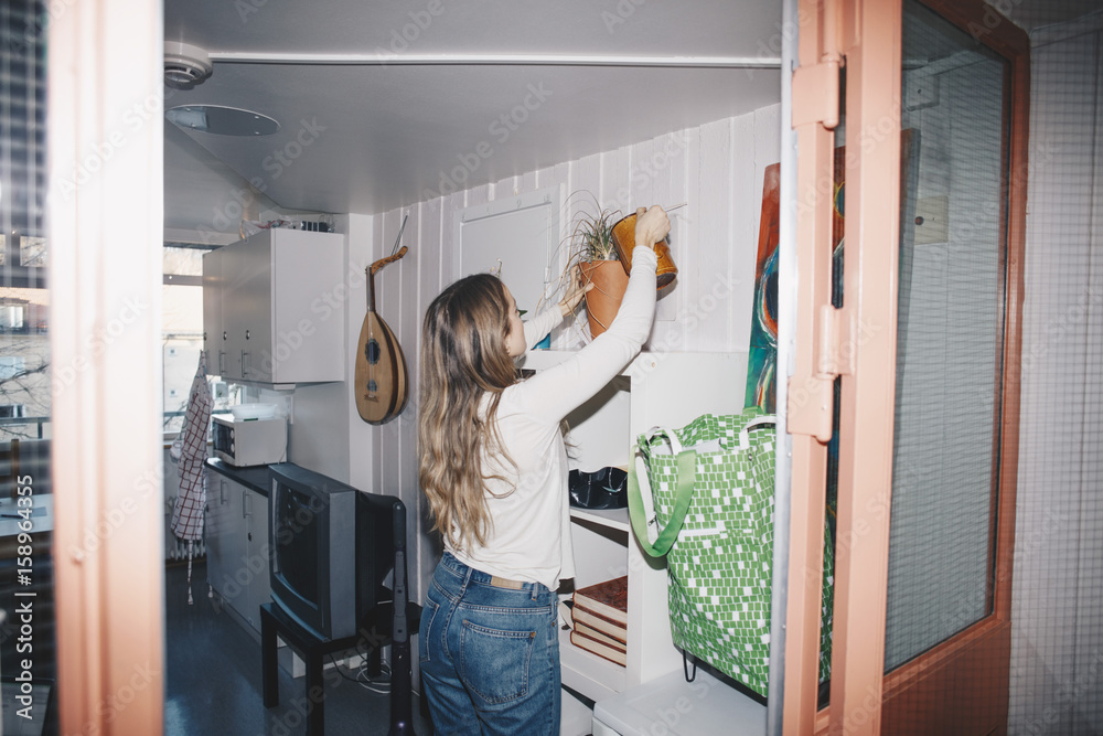 © Maskot - Woman watering potted plant in dorm room