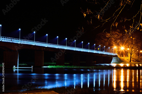 Most nad rzeka w nocy oświetlony latarniami.