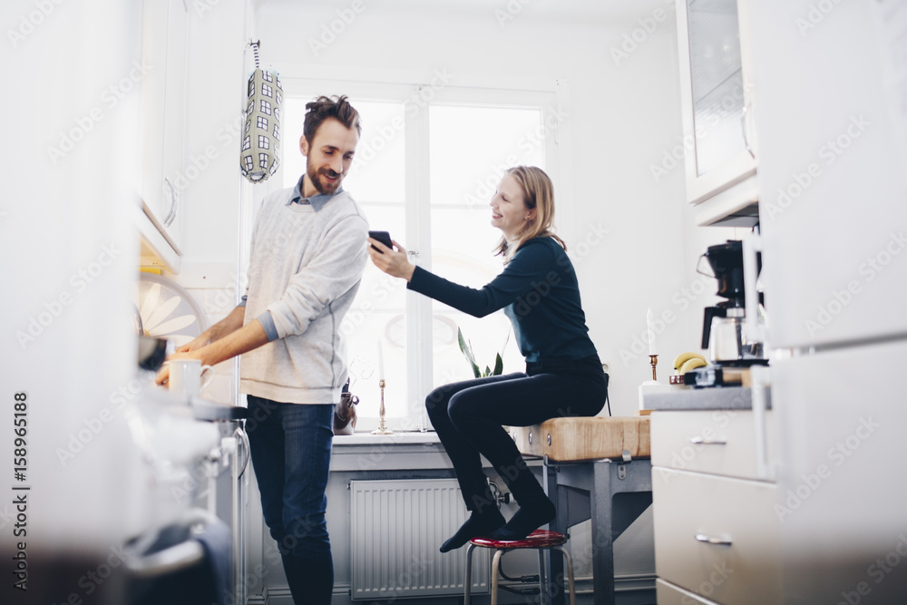 Happy woman showing mobile phone to man in kitchen at home