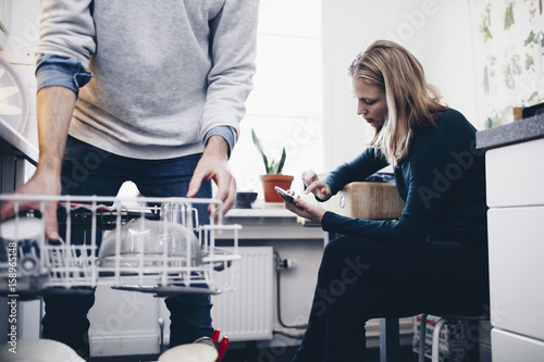 Midsection of man working in kitchen with woman using mobile phone at home photo