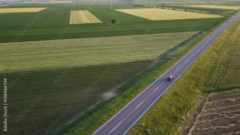 Aerial view of cars on the road through cultivated countryside, drone pov