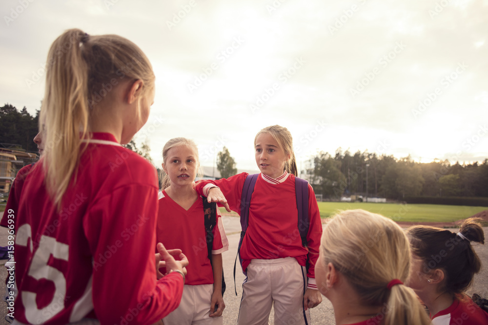 Girls wearing red soccer uniform talking against sky Girls wearing red soccer uniform talking against sky