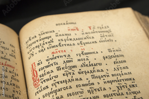 Open book with light spotlight on text. Reading of opened book educate reader. Ancient Bible text reading on black background. Russian bible. Red initial letter in slavonic text.