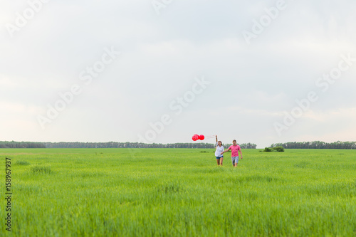 Man and woman on the field with red balloons. Happy couple on nature © satura_