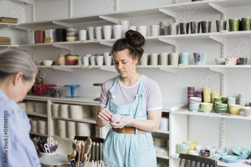 Young female potter holding clay with senior colleague against vases on shelf at workshop photo