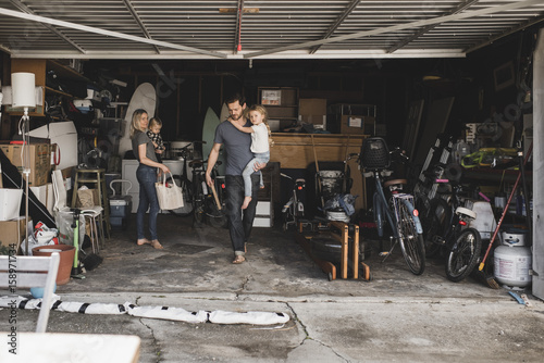 Mid adult parents carrying children while working in storage room at garage photo