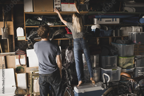 Rear view of man looking at woman arranging boxes on shelf in storage room