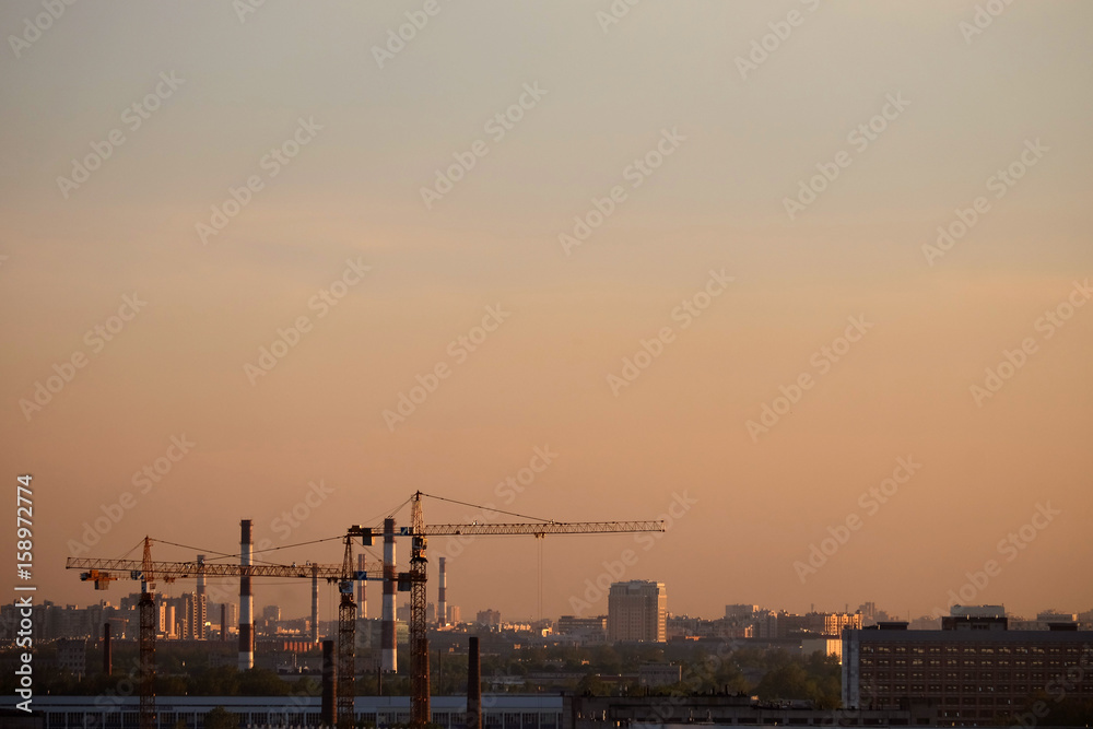 Photo of a building process in the city in the evening. Cranes and pipes.