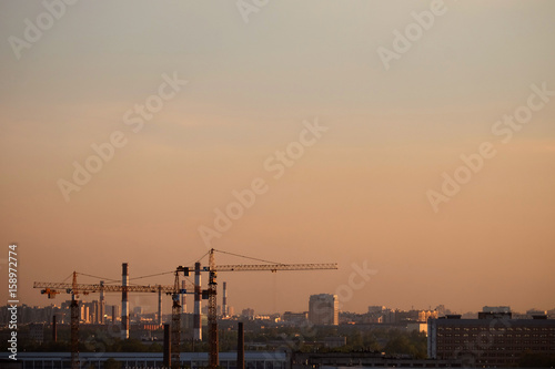 Photo of a building process in the city in the evening. Cranes and pipes.