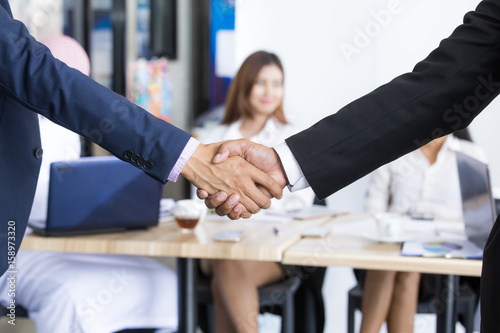 Businessmen handshaking after striking grand deal while meeting with team.