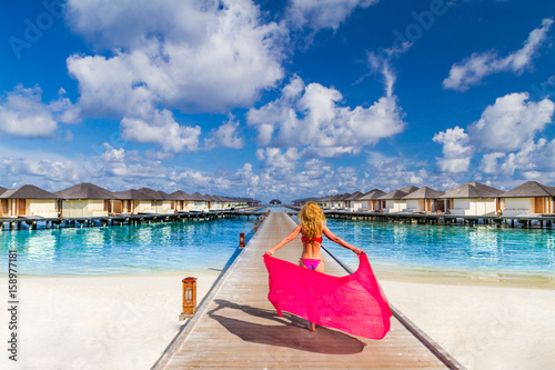 Outdoors lifestyle fashion portrait stunning girl walking on the beach luxury resort background. Wearing stylish bikini with pink scarf. Straight blonde long hair. Enjoying life in paradise beach sea © icemanphotos