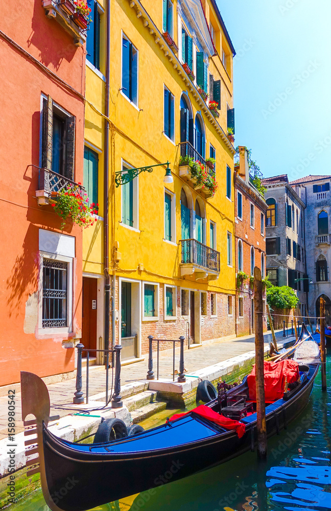 Picturesque view of gondola moored on peaceful narrow canal in front of colorful buildings in Venice, Italy
