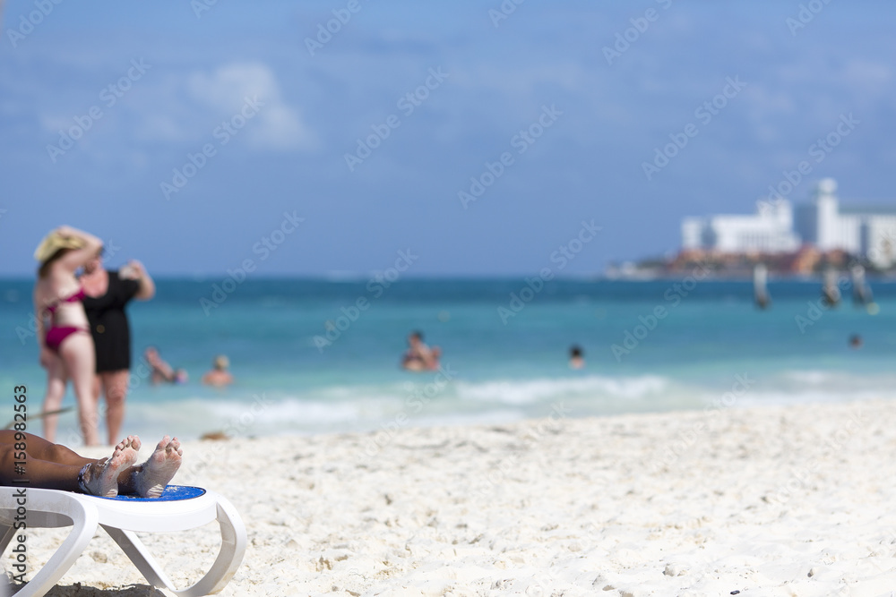 People on the beach on a sunny day. The Caribbean sea shore. Focus point on the toes in left. Copy space.