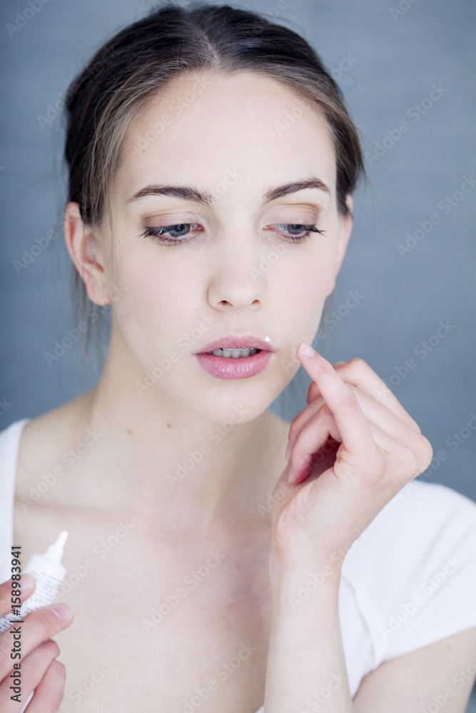 Woman applying cream to treat labial herpes Woman applying cream to treat labial herpes