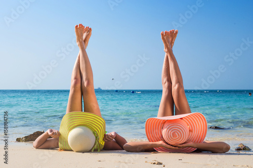 Girls sunbathing on the sea. Girlfriends have a rest on the beach. Long legs of young girls on the beach. Relax on vacation. Sexual girls lying on the seashore.