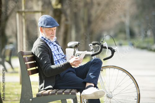 Senior man on bench with bicycle and smartphone, texting.