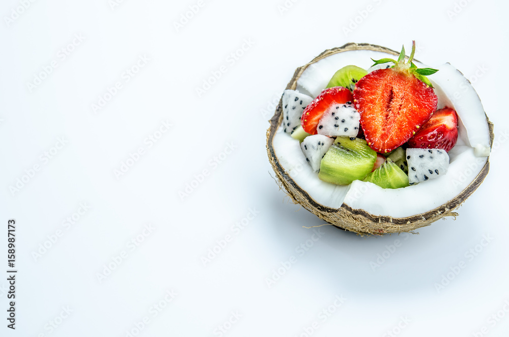 Pieces of strawberries, kiwi and dragon fruit in a half of coconut.
