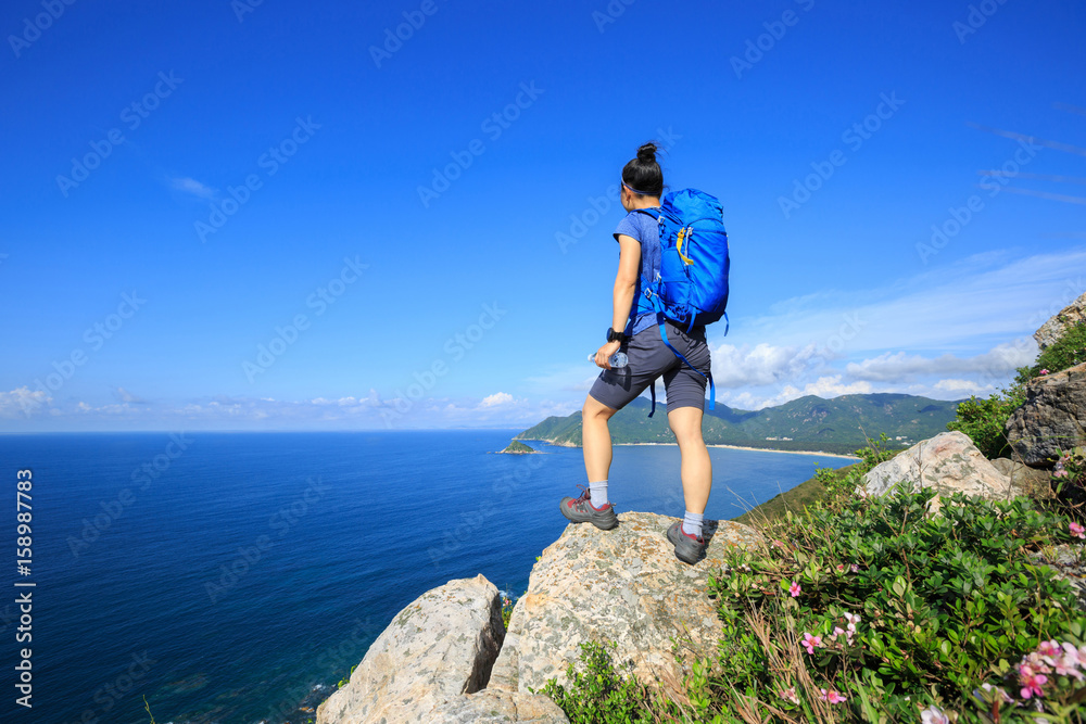 Naklejka premium successful woman backpacker enjoy the view on seaside mountain rock