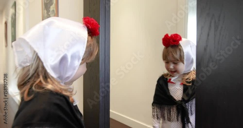 three years old girl disguised as typical and traditional costume of Madrid city, in Spain, with carnation flower, headscarf and dress, looking in the mirror smiling, for festivity La Paloma
