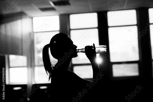 Resting time. Silhouette of sporty girl drink water. Photo of fitness model. Health concept. photo
