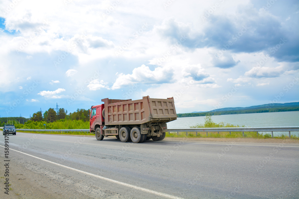 A dump truck is driving along the highway in summer