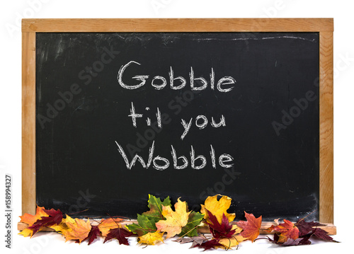 Gobble tip you wobble written in white chalk on a black chalkboard decorated with autumn fall leaves isolated on white