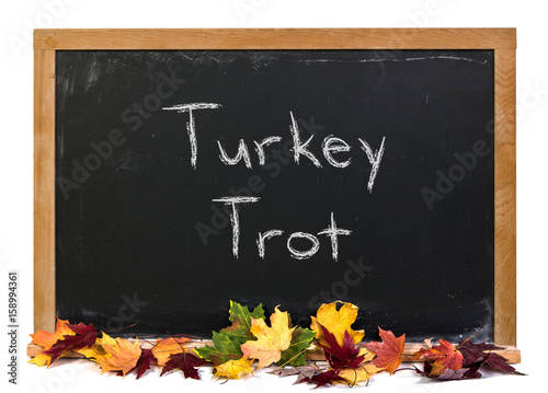 Turkey Trot written in white chalk on a black chalkboard decorated with autumn fall leaves isolated on white