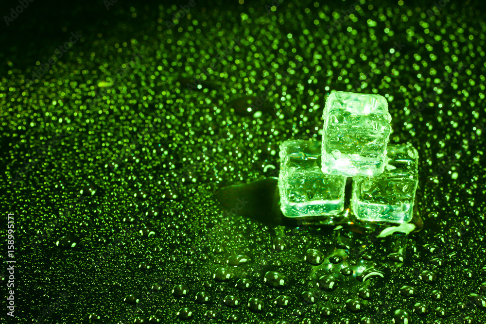 Ice cubes in green light on black wet table.