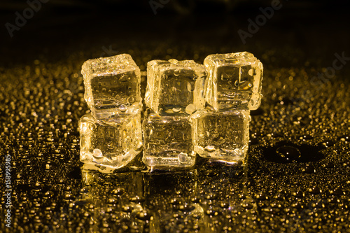 Ice cubes in yellow light on black wet table.