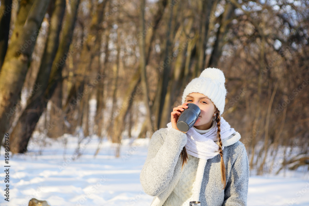 Young woman drinking a mug of tea in the forest on natural background, in a campaign, looking into the camera