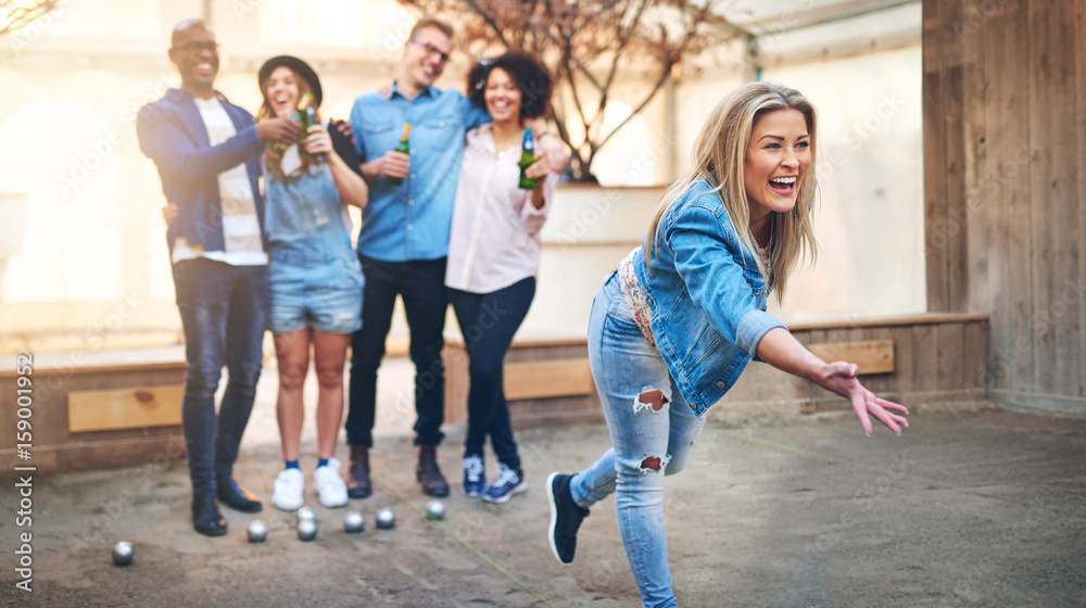 Young woman throwing petanque ball playing with friends