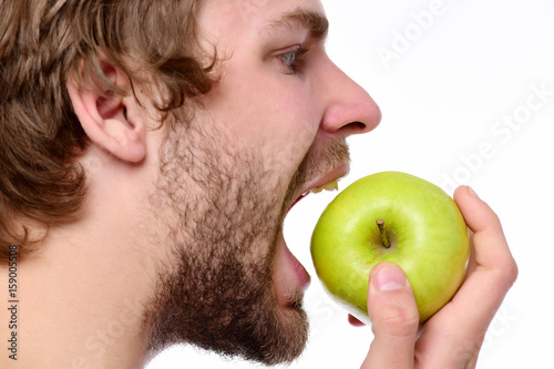 Guy trying to bite big green apple looking at it photo