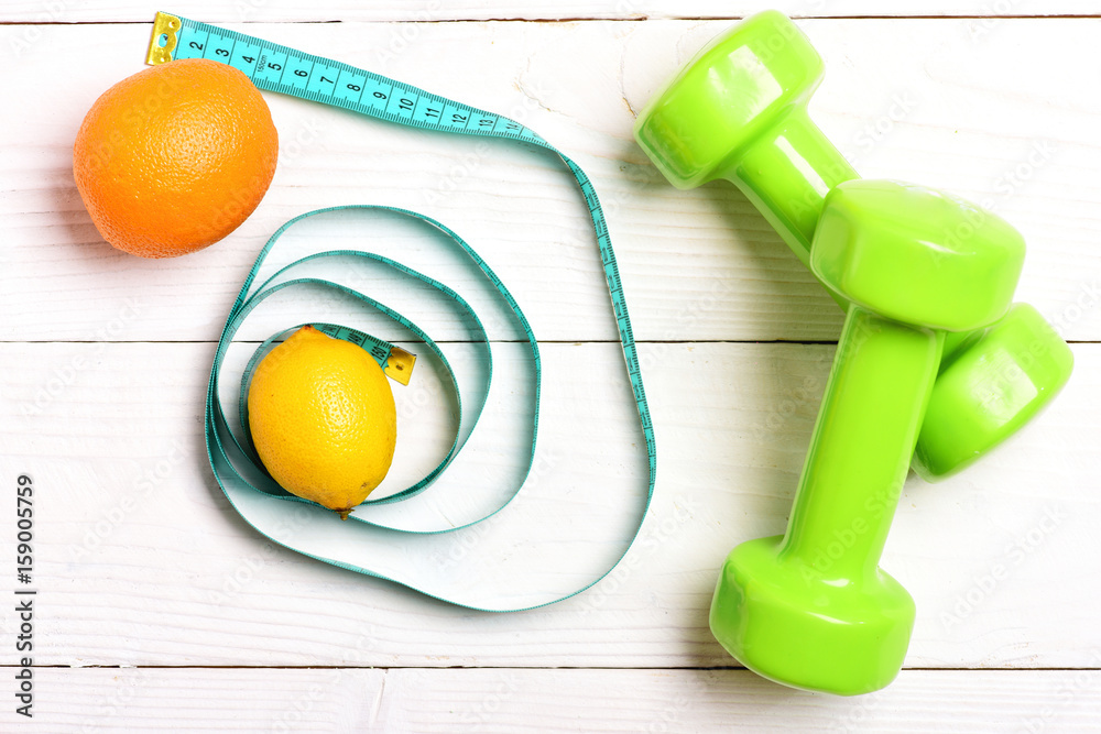 Lemon and orange fruit in cyan measuring tape near dumbbells Lemon and orange fruit in cyan measuring tape near dumbbells