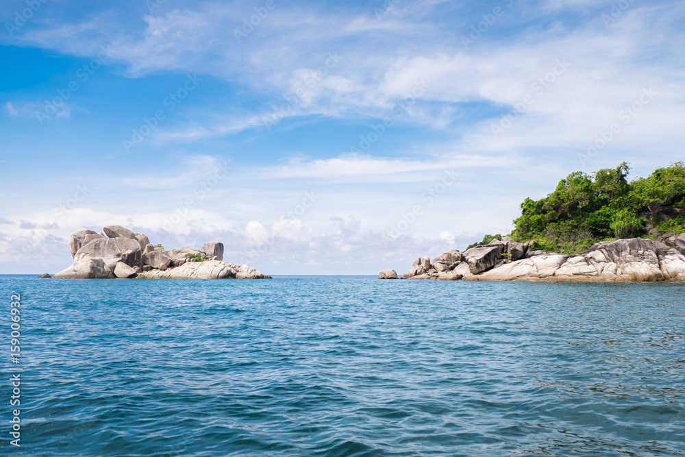 Summer sea in Thailand with. Islands are under bright blue sky and a space between the islands with trees and no trees. Clouds are floating slowly above the dark blue sea. 