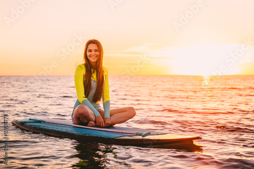 Stand up paddle boarding on sea with warm summer sunset colors. Happy smiling girl on board at sunset © artifirsov