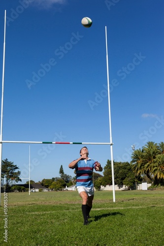 Full length of rugby player catching ball against blue sky