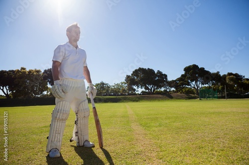 Cricket player with bat standing on grassy field