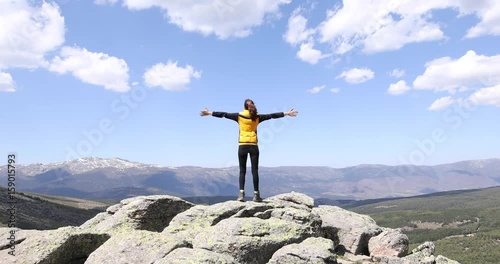 sport hiking or trekking woman with yellow jacket, standing back on rock peak, with arms up outstretched, behind Lozoya Valley and Guadarrama Park, in Madrid, Spain
 photo