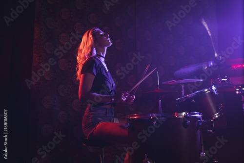 Foto Young female drummer performing in illuminated nightclub