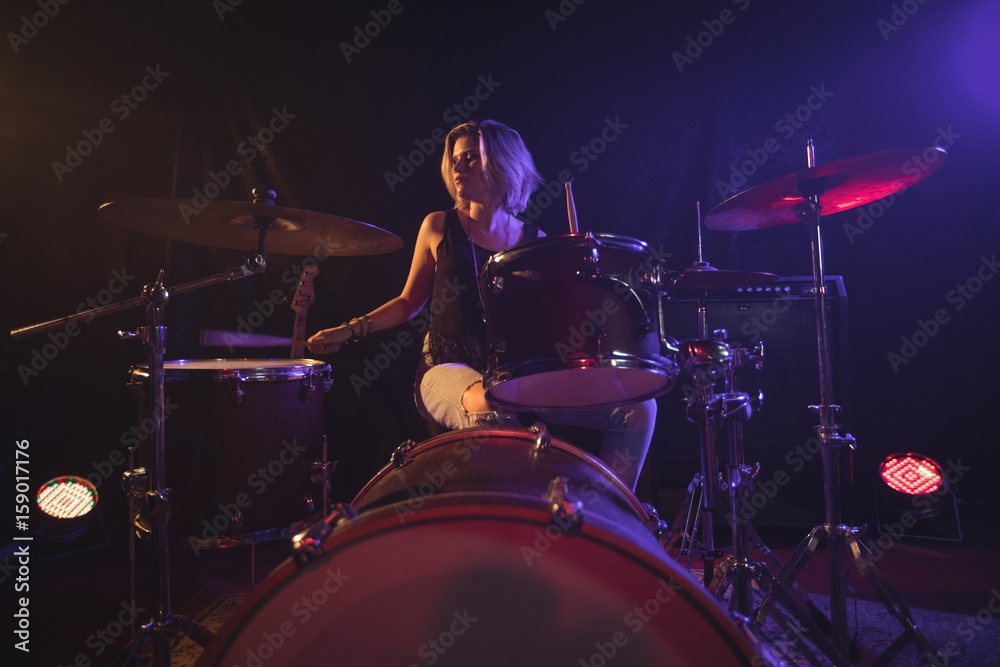 Female drummer playing drum kit in illuminated nightclub