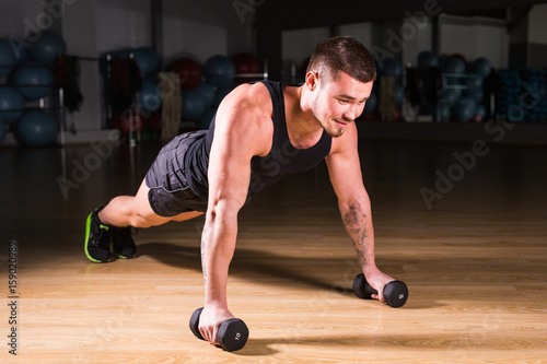 Young Man Athlete Doing Pushups With Dumbbells As Part Of Bodybuilding Training.