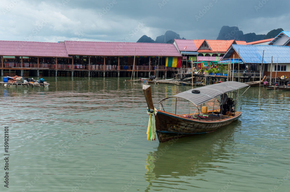 Longtail boat with houses and rainclouds in the background Longtail boat with houses and rainclouds in the background