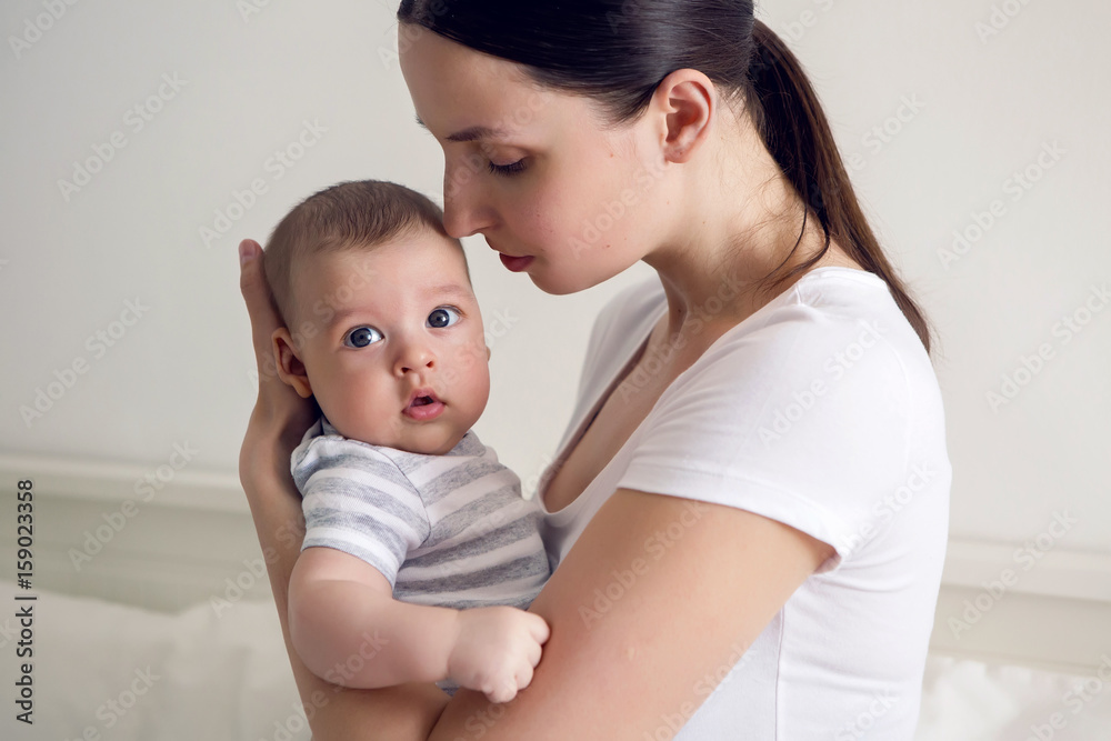 mother with her newborn son in hands sitting on a big white bed mother with her newborn son in hands sitting on a big white bed