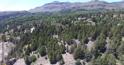 Aerial drone scene of houses in the woods in mountain in south Patagonia, Argentina, city of San Martin de los Andes with Chapelco mountain on the background. Windy day and trees moving. photo