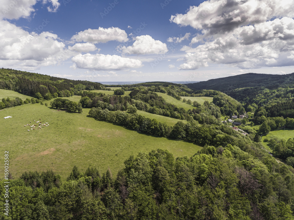 Fototapeta premium Aerial view of the summer time in mountains in border Poland and Czech Republic. Pine tree forest and clouds over blue sky. View from above.