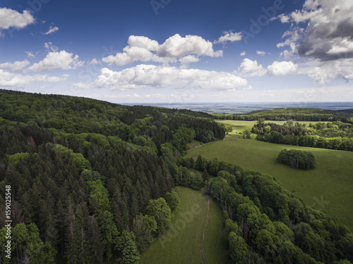 Aerial view of the summer time in mountains in border Poland and Czech Republic. Pine tree forest and clouds over blue sky. View from above.